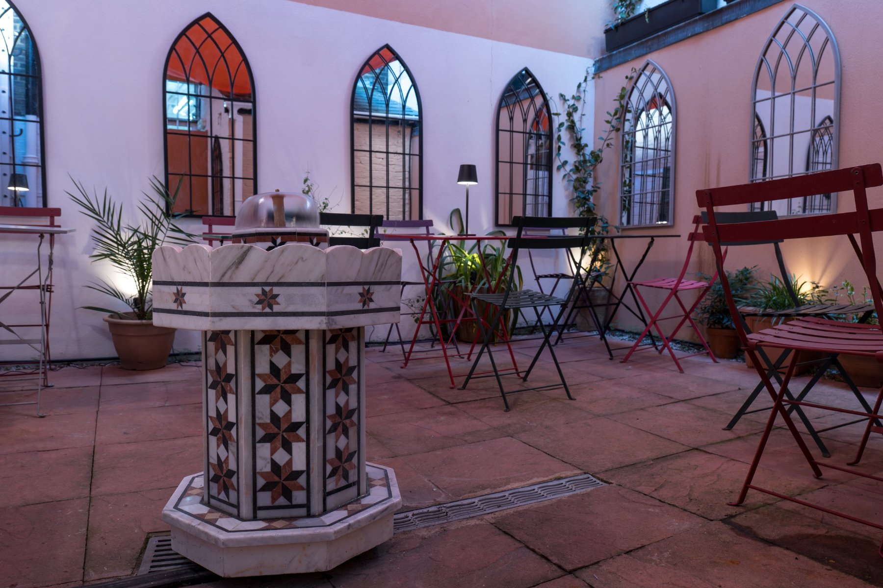 The courtyard garden at night, with a tiled fountain, arched windows and café tables